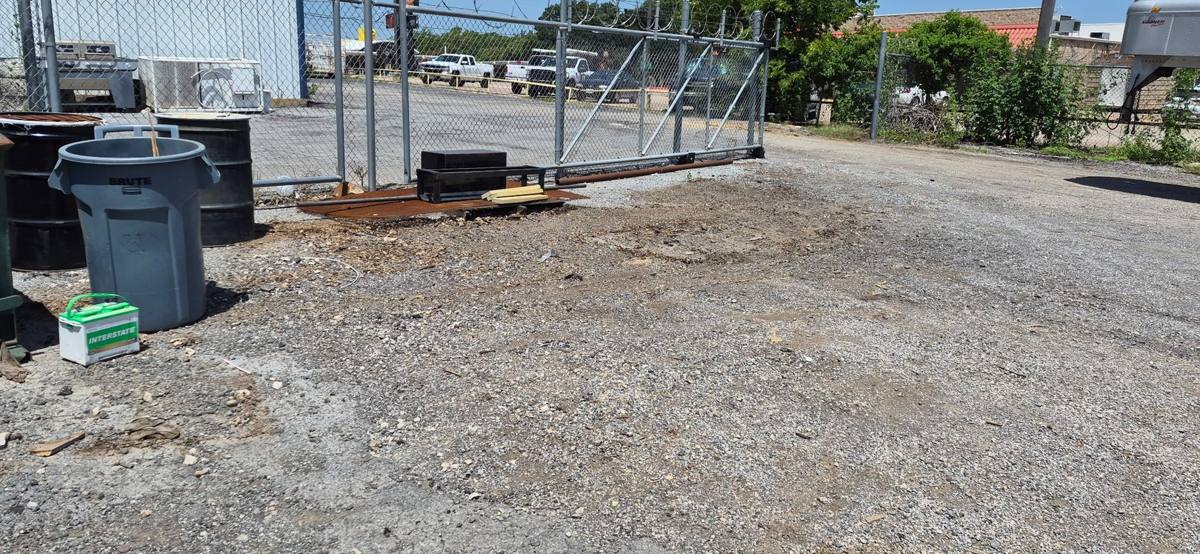 Gravel work area at a commercial property with bins and chain-link fencing